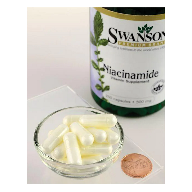 A small bowl of white capsules sits beside a penny on a clear surface, with a bottle labeled "Swanson Niacinamide (Vitamin B3) 500 mg 250 Capsules" in the background.