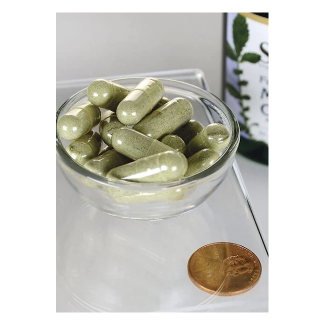 A small glass bowl holds green capsules full of antioxidants, with a penny for scale. In the background, a partially visible bottle featuring a leaf design indicates Swanson's Full Spectrum Moringa Oleifera 400 mg capsules, known for their beneficial phytonutrients.