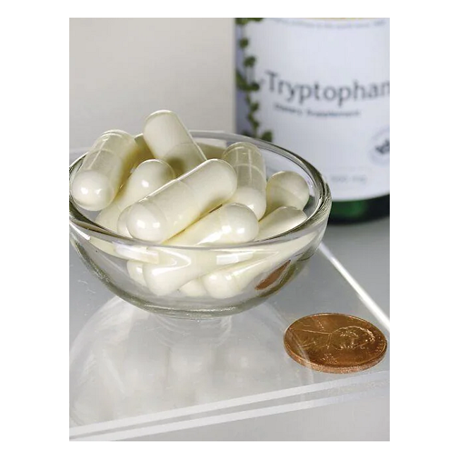 A small glass bowl of white capsules sits next to a penny for scale, with a Swanson L-Tryptophan 500 mg 60 Capsules bottle in the background. This essential amino acid is noted for promoting restful sleep.