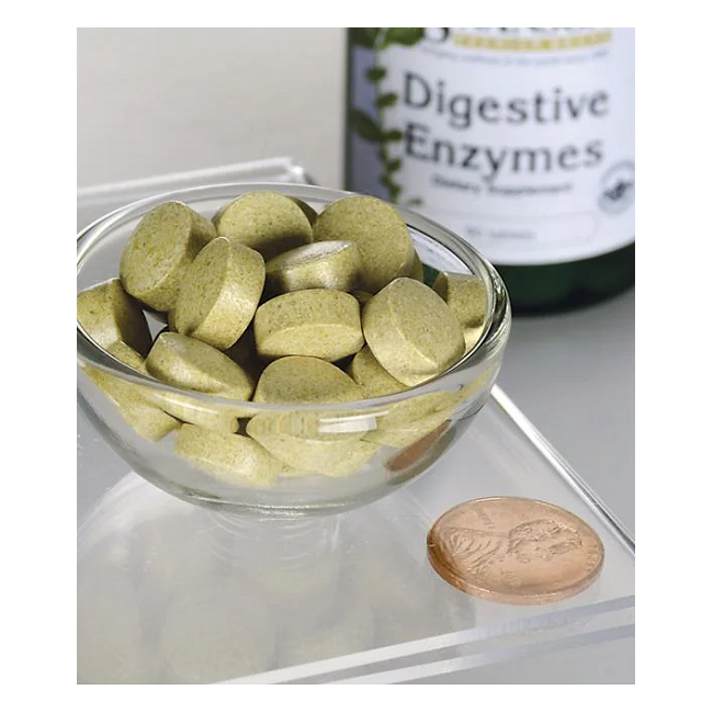 A small glass bowl holds green tablets known for digestion support, placed next to a brown coin. Nearby, a Swanson "Digestive Enzymes 90 Tablets" bottle underscores a holistic approach to health.