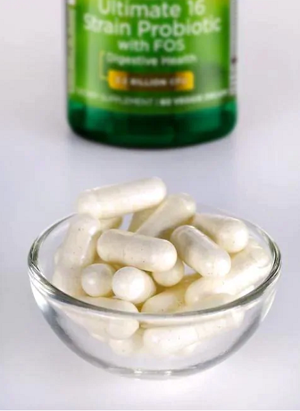 A small glass bowl of white capsules sits in front of a green bottle labeled "Dr. Stephen Langer's Ultimate 16 Strain Probiotic with FOS" by Swanson, promoting intestinal health.