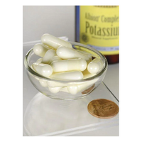 Thumbnail for A small glass bowl filled with white capsules is shown next to a penny for scale. In the background, a blurred bottle of Swanson's Albion Potassium 99 mg 90 Capsules promises electrolyte balance support.