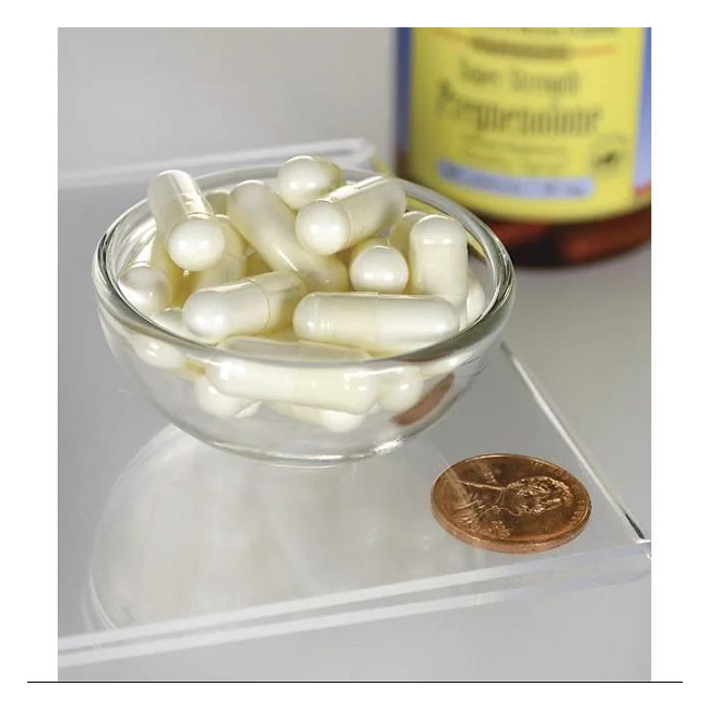 A small glass bowl holds white capsules, likely from Swanson's Pregnenolone 50 mg Super Strength. A penny is nearby, and a supplement bottle with a blurred label is visible in the background.