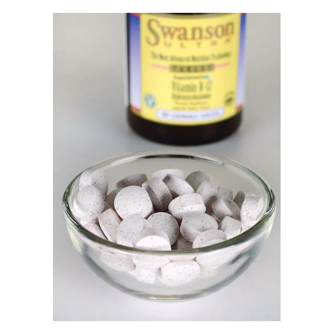 A glass bowl filled with round white tablets is in front of a blurred Swanson Vitamin B-12 - 1000 mcg 60 tabs Hydroxycobalamin bottle, suggesting its essential role in energy production.