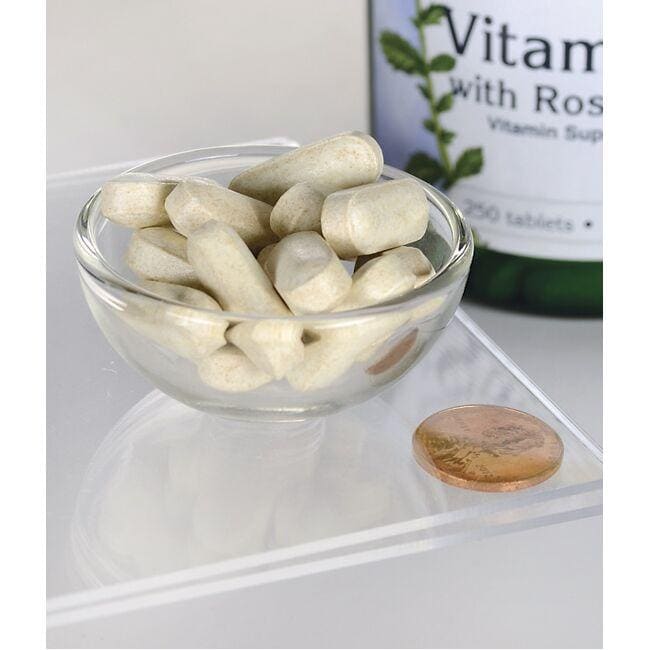 A glass bowl of Swanson's Vitamin C with Rose Hips - 1000 mg 250 Tablets on a white surface with a bottle labeled "Vitamin C with rose hips for Antioxidant Support" in the background.