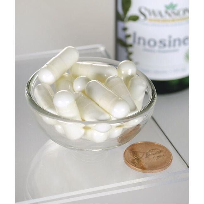 Un bol de pastillas blancas junto a un frasco de Swanson Inosina - 500 mg 60 cápsulas vegetales.