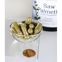 Miniatura de Swanson Saw Palmetto - 540 mg 250 cápsulas, conocidas por su papel en el fomento de la salud de la próstata y la fluidez de las vías urinarias, se muestran en un cuenco junto a un penique.