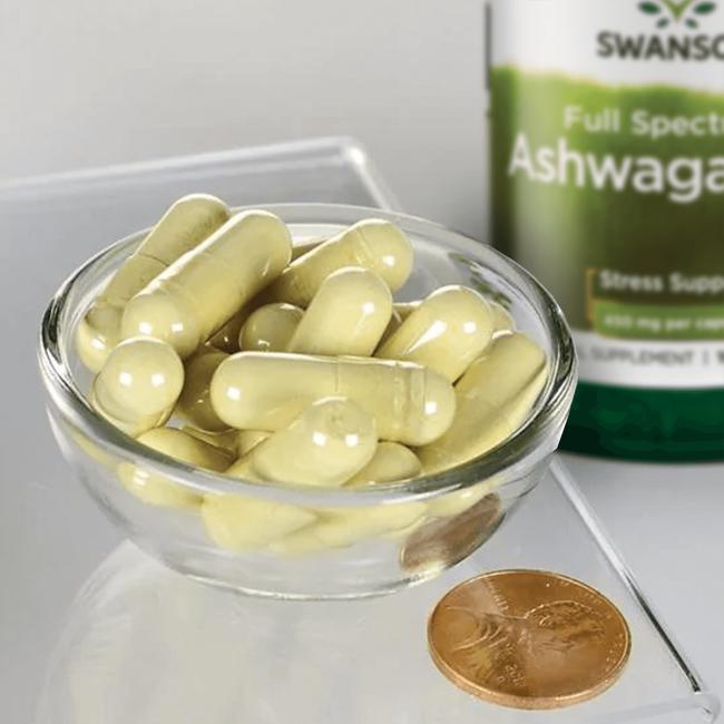 Un cuenco de Swanson Ashwagandha - 450 mg 100 cápsulas con una moneda al lado.