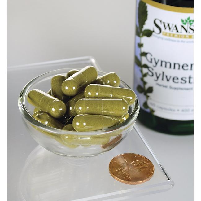 Un frasco de Swanson Hoja de Gymnema Sylvestre - 400 mg 100 cápsulas con un penique en un cuenco.