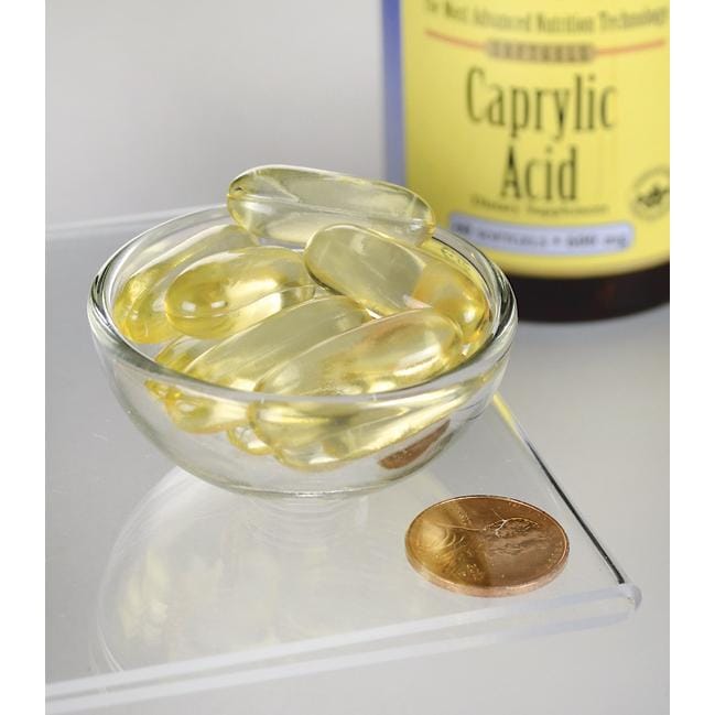 Swanson's Caprylic Acid - 600 mg 60 cápsulas de suplemento dietético de gelatina blanda en un cuenco junto a una moneda.