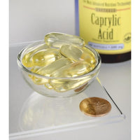 Miniatura de Swanson's Caprylic Acid - 600 mg 60 softgel dietary supplement capsules in a bowl next to a coin.